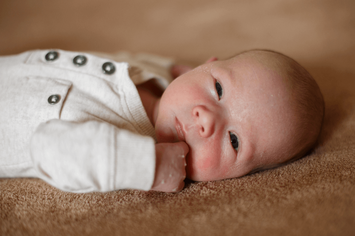 Foto de um bebê prematuro deitado com a mão esquerda na boca